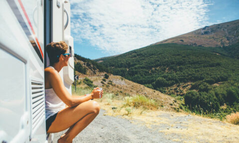 Side view of a young woman is sitting on a caravan step and holding a cup on a holiday adventure trip stop. Copy space area available